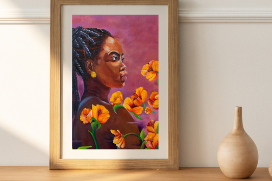 A framed artwork featuring a stylized black woman with orange flowers, placed on a wooden surface.